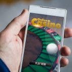 Mensch hält Smartphone mit Roulette-Spiel in der Hand