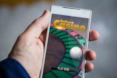 Mensch hält Smartphone mit Roulette-Spiel in der Hand