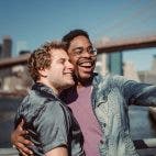Zwei menschen lächeln, Skyline und Brücke im Hintergrund. Handy, Selfie, Smartphone, Couple, Männer, Foto von Ketut Subiyanto von Pexels