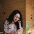 Person, lange dunkle Haare, lächelt, Smartphone in der Hand Flasche auf dem Tisch. Foto von Airam Dato-on auf Unsplash