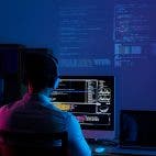 Mensch mit Kopfhörern vor Monitor mit Codezeilen